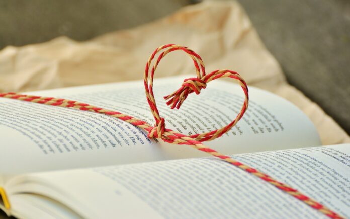 Un libro aperto e sopra un cordino rosso intrecciato forma un cuore