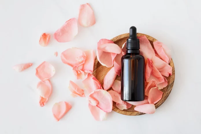 Olio di jojoba, pelle, oli essenziali, benefici, cura. Un olio con intorno dei petali di rosa rosa.