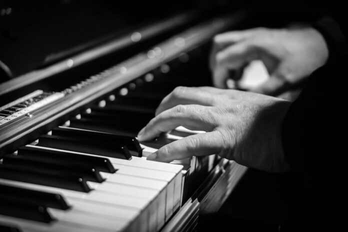 magnitudo - foto in bianco e nerro con due mani distese sopra la tastiera di un pianoforte