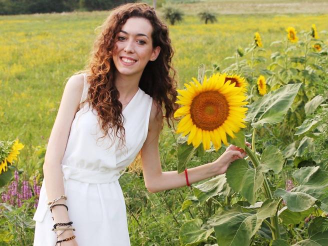 Insieme tra le righe - un'autrice Sara Cornelio vestita di bianco, ha lunghi capelli ricci e rossi, è in un campo di girasoli, Sara ne tiene uno in mano