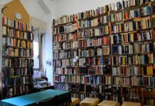 biblioteca di condominio libri in una portineria su pareti alte fino al soffitto un tavolo verde e sedie intorno