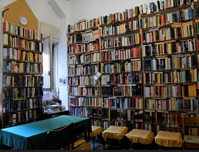 biblioteca di condominio libri in una portineria su pareti alte fino al soffitto un tavolo verde e sedie intorno