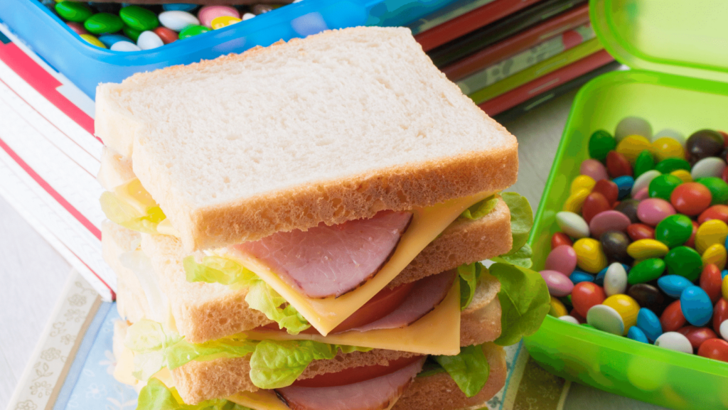 obesita infantile anche cuasusa solchi sigilaltura in foto panino con quatto strati e caramelle multicolori appoggiate su una colonna di libri e quaderni