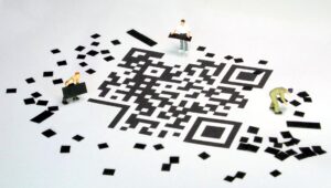 Credito sociale - nella foto degli omini tipo "playmobil" cosruiscono per terra su sfondo bianco un qr code con dei lego neri
