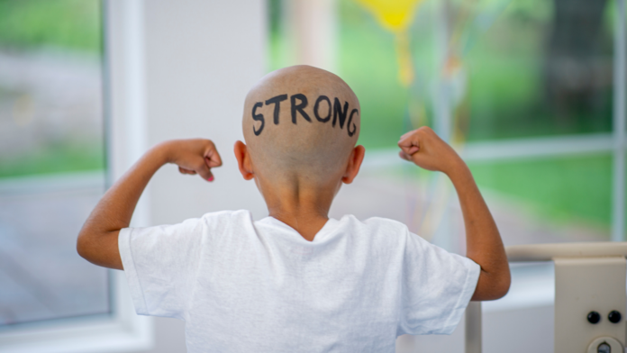 Un bambino affetto da tumore con i capelli rasati tasti e la scritta strong sul capo