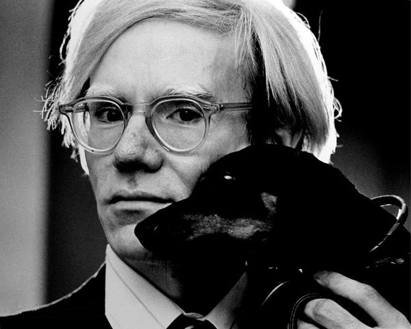 andy wharol fotografato a mezzo busto in bianco e nero con il suo cane appoggiato al colllo