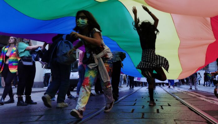persone che ballano lungo la strada sotto una bandiera arcobaleno simbolo del pride queer e ora
