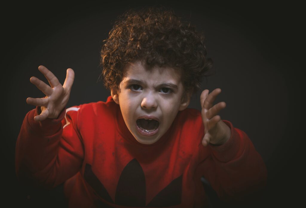 violenza domestica e parental abuse: un bambino con felpa rossa e tanti ricci urla agitando le mani in avanti