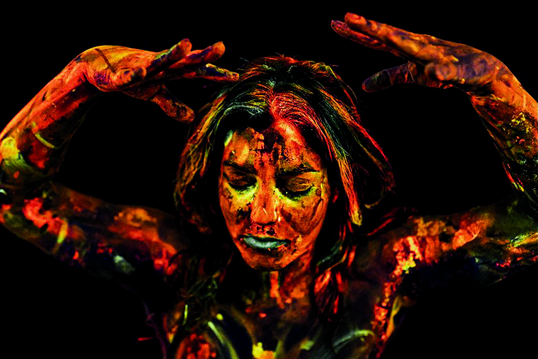 una danzatrice indiana Yaraka con viso dipinto toni arancio e verde e nero durante una perfomance