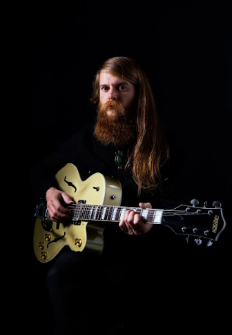 vision - black snake moan in primo piano con una chitarra tra le braccia. capelli e barba lunghi e rossicci, è vestito di nero