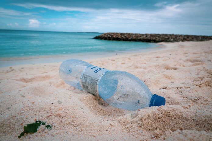 plastic free july - una bottiglia di plastica sulla spiaggia e, dietro, il mare
