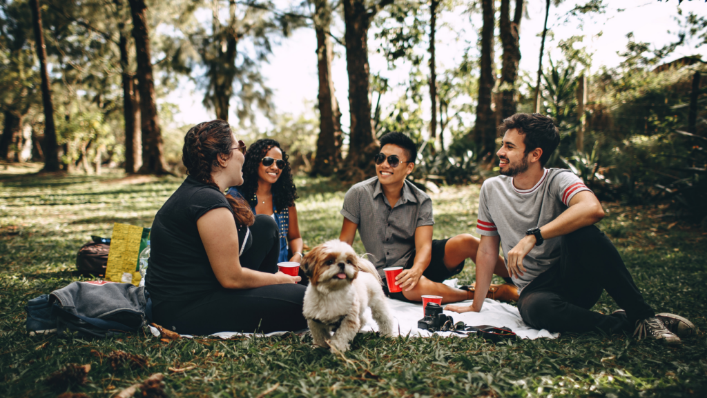 un gruppo di persone sorridenti su un prato con un cane mentre fa un picnic