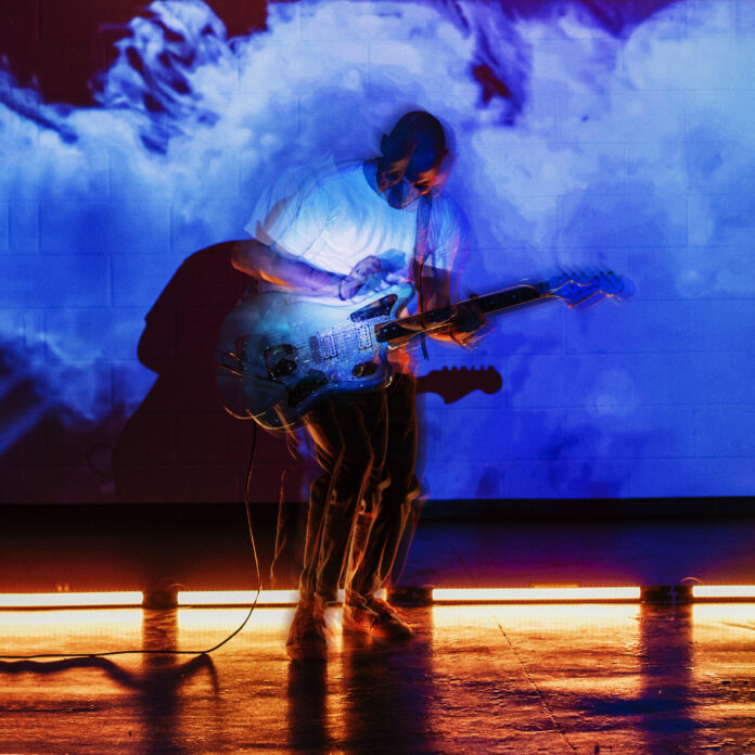 tolkins in una immagine dall'effetto sfocato, imbraccia una chitarra elettrica