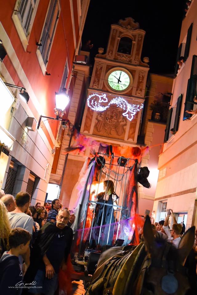 Festa delle Basüe - nella foto tanta gente di schiena in un corteo. Sono vestiti dcon un mantello bianco con cappuccio e seguono un carro 