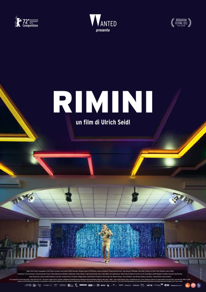 rimini - la locandina del film con un palcoscenico illuminato dai riflettori e il cantante al centro da solo. Sppra il palco ci sono dei neon colorati