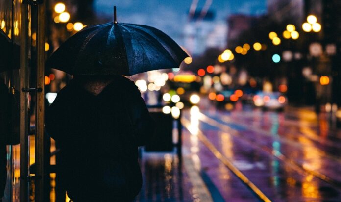 scirocco - una persona con l'ombrello sotto la pioggia, di sera in città