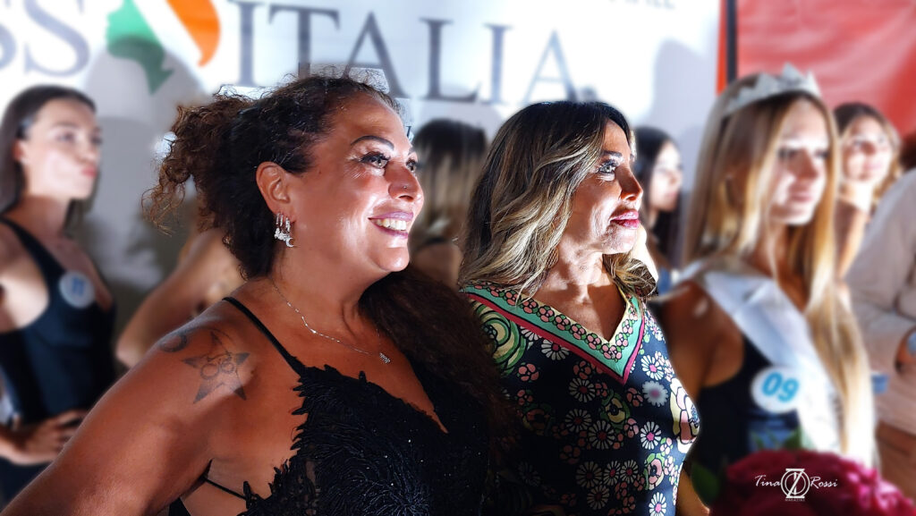 A sinistra Barbara con capelli ricci lunghi raqccolti in uno chinon, indossa un vestito con bretelline nero con strass, sulla destra Mirella Rocca con lunghi capelli biondi e un vestito estivo colorato con fiori