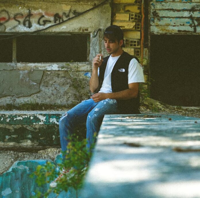 grigia provincia - spera, indossa jeans, t shirt bianca e gilet nero, è seduto su un muretto