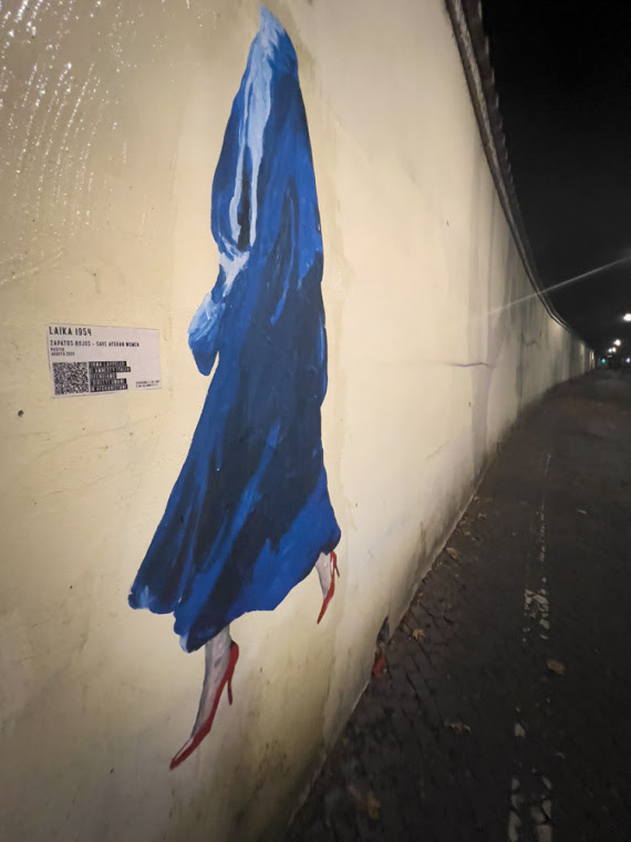 vioolenza contro le donne - su un muro di Roma il disegno di una donna afghana vestita con un abito blu e il burqa. La donna indossa scarpette rosse, simbolo della lotta contro la violenza sulle donne nella foto l'opera di street art con 