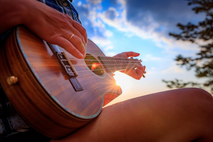 canzoni dell'anima al Cantacielo - nella foto il primo piano di una chitarra nelle mani di un ragazzo che suona sotto un cielo assolato con nuvole bianche
