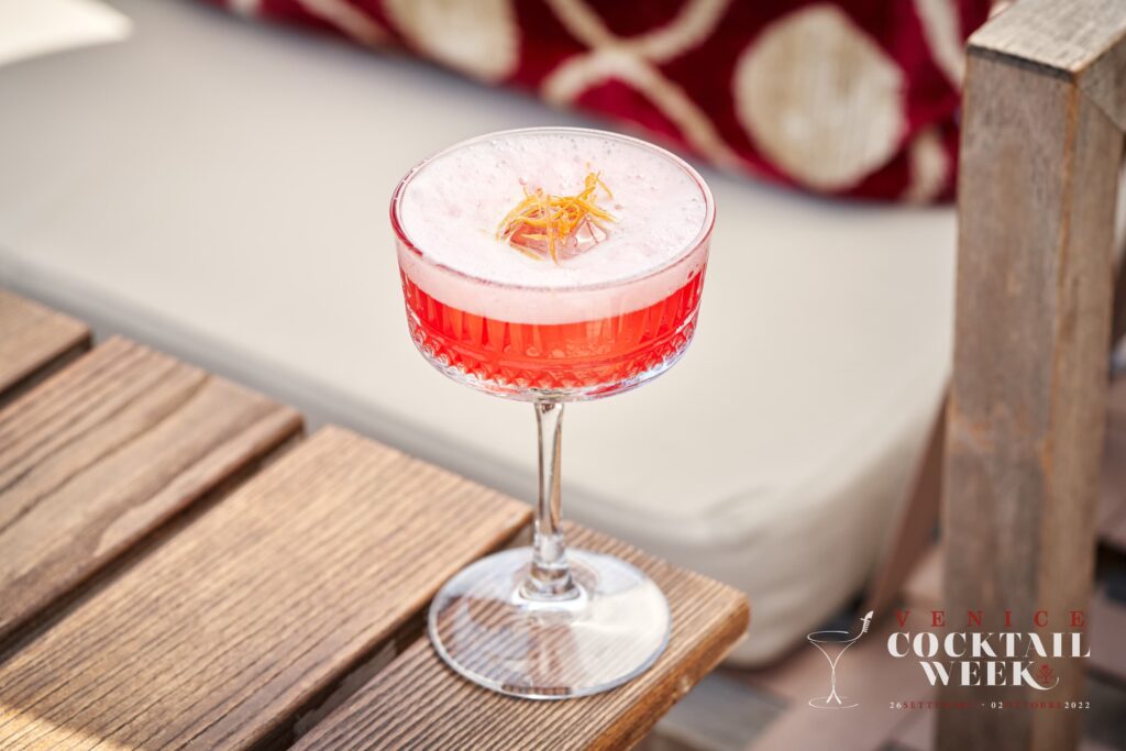 Venezia - Venice Cocktail Week - un Bicchiere con un drink rosso con la spuma bianca sopra e il logo della VCW