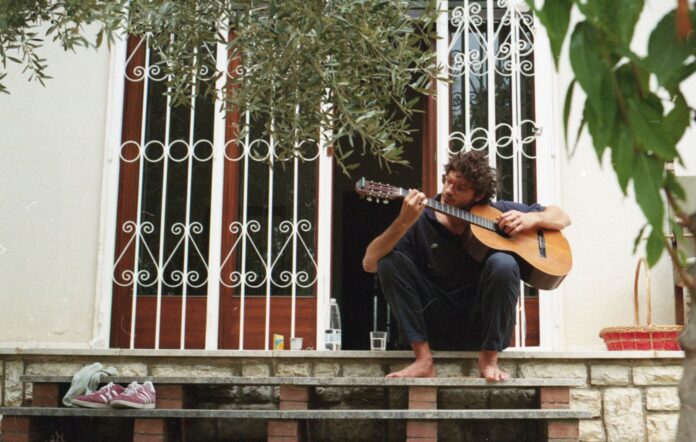 giovanni toscano è seduto sui gradini di casa, davanti a una porta-finestra, intento a suonare la chitarra