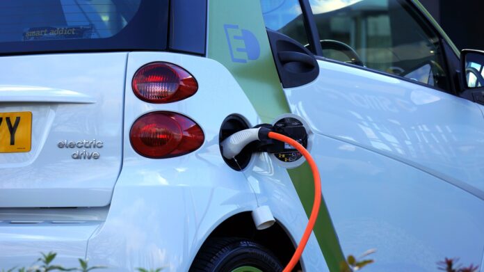 auto elettrica - nella foto in primo piano un' auto bianca e la spina di ricarica infilata nella presa