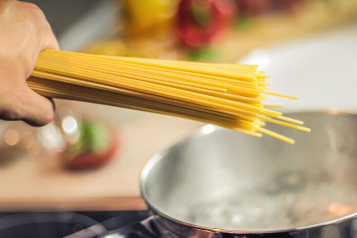cucinare la pasta - nella foto una prersona sta mettendo degli spaghetti in una pentola contenente acqua che bolle