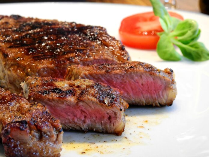 Un piatto con una bistecca tagliata a fette una ftta di pomodoro e un ciuffo di insalata