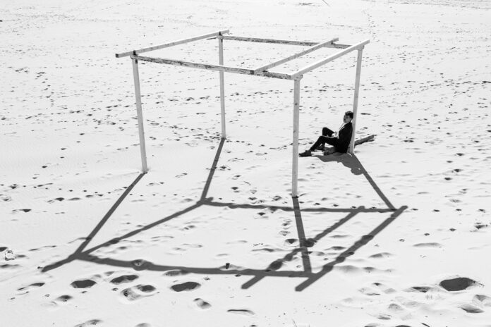 giorgio mannucci - un uomo vestito di scuro, appoggiato ad una struttura in legno sulla spiaggia