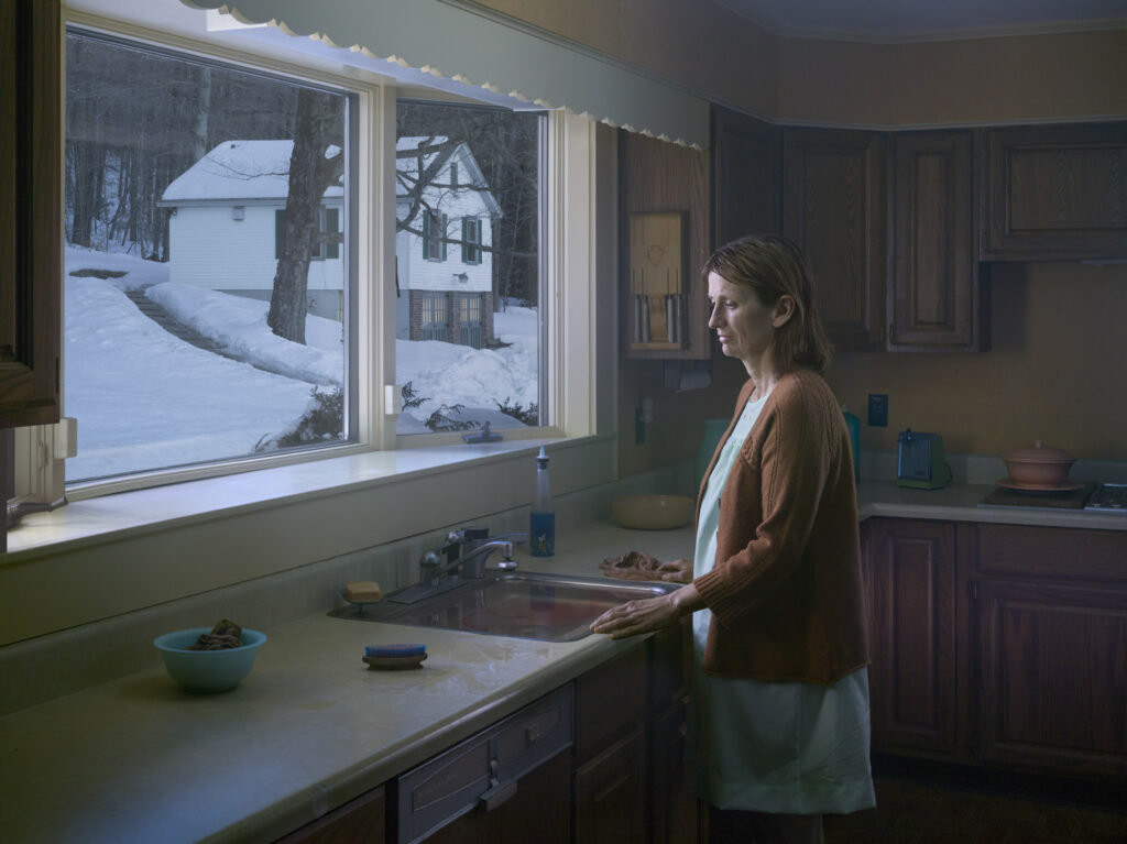 una donna vicino al lavello di una cucina con davanti una finestra con paesagggio innevato