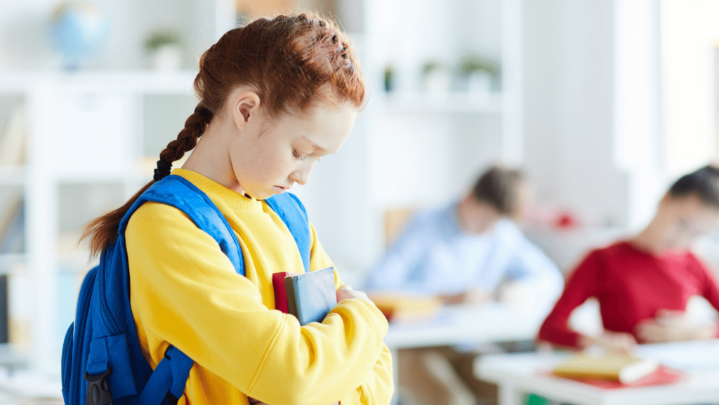 una bambina con maglia gialla a capo chino triste stringe i suoi quaderni