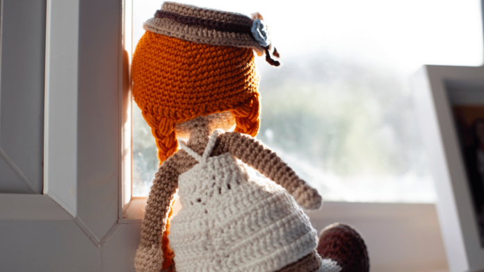 una bambola all'uncinetto di fronte a una finestra in solitudine