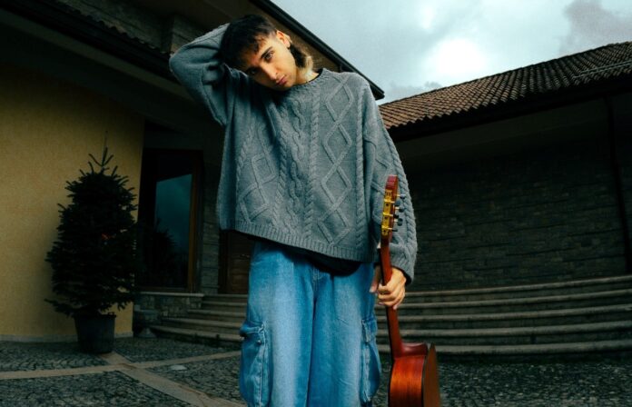 frada in primo piano, indossa jeans sformati axzzurri, maglione grigio e ha una chitarra nella mano sinistra