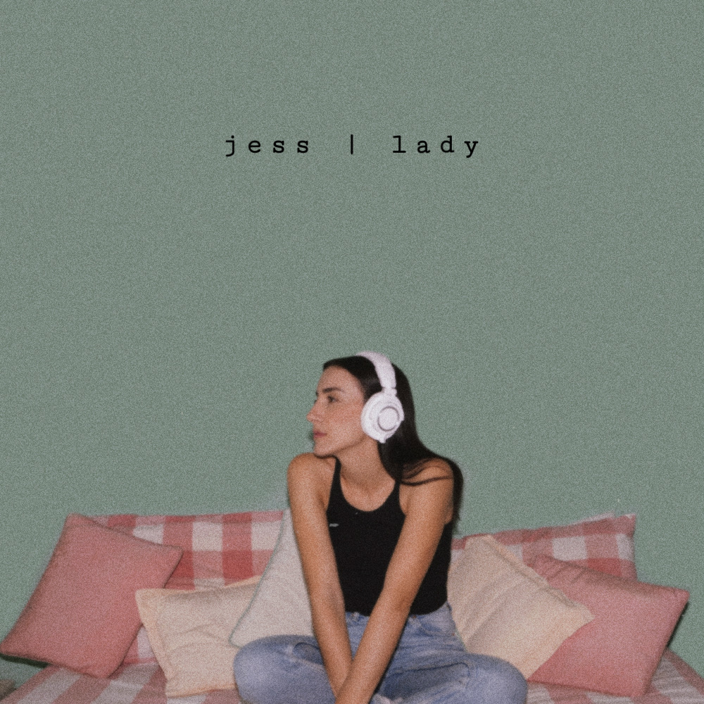 lady - la copertina del singolo che vede jess seduta su un divano coi cuscini rosa. idossa jeans chiari e cantta ner e ha le cuffie in testa