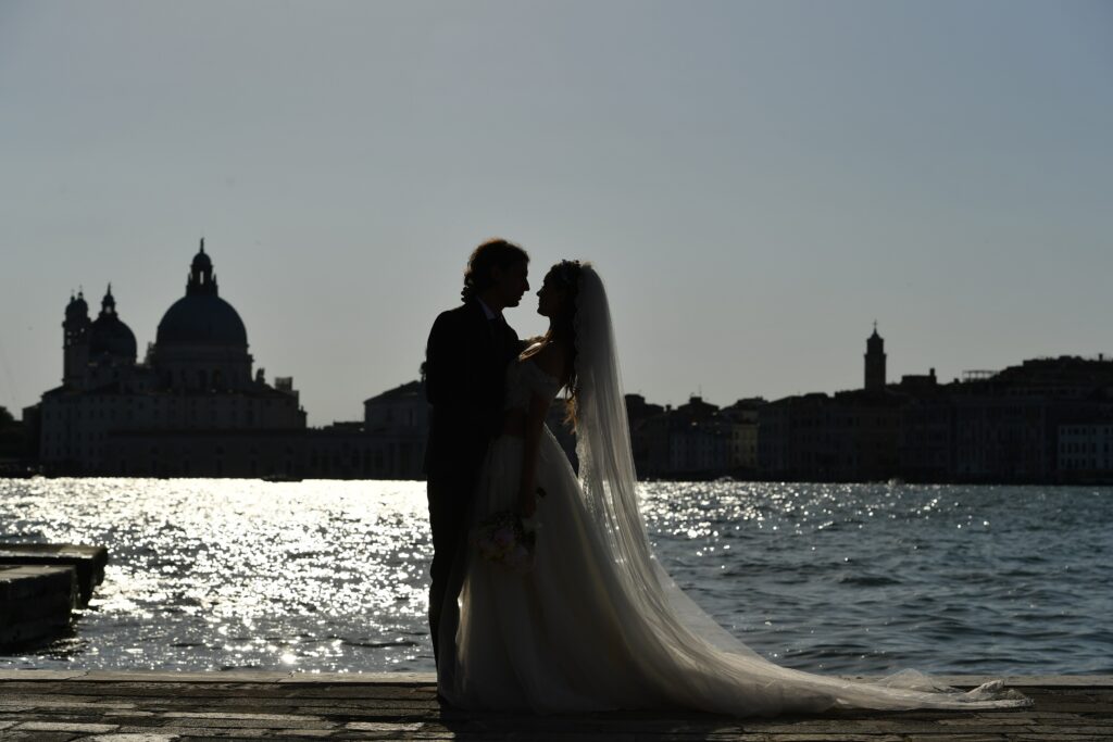 Venice Wedding -  una coppia di sposi in piedi davanti alla laguna sui cui scende la sera