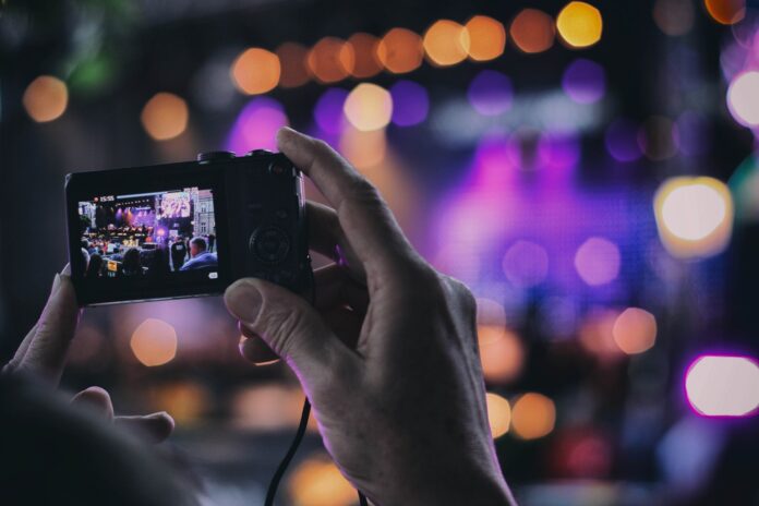 eventi culturali - un concerto di musica con tante luci colorate e in primo piano due mani tengono un cellulare che sta filmando