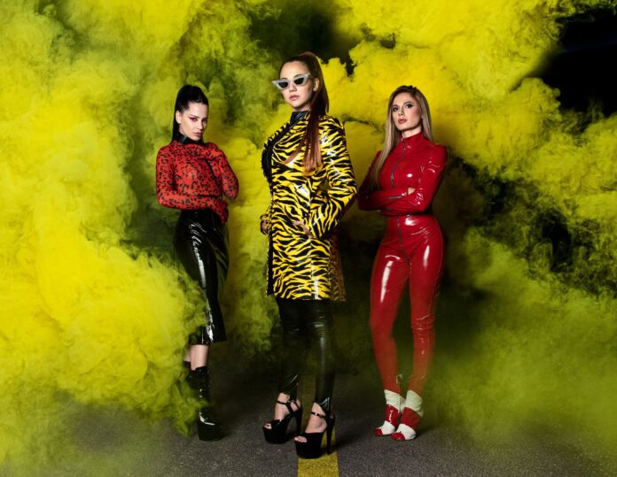 le tre ragazze della band luci al neon in primo piano, avvolte da fumo giallo