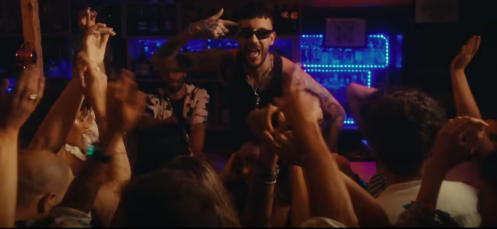 fred de palma in un frame del video Extasi un ragazzo con occhiali scuri con canottiera nera in una discoteca cha fa reggaeton circondato da molti altri ragazzi e ragazze