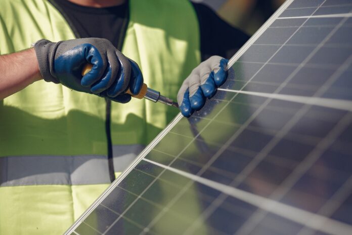 fotovoltaico - nella foto un pannello solare e un uomo vestito da operaio con guanti spessi sta avvitando una vite