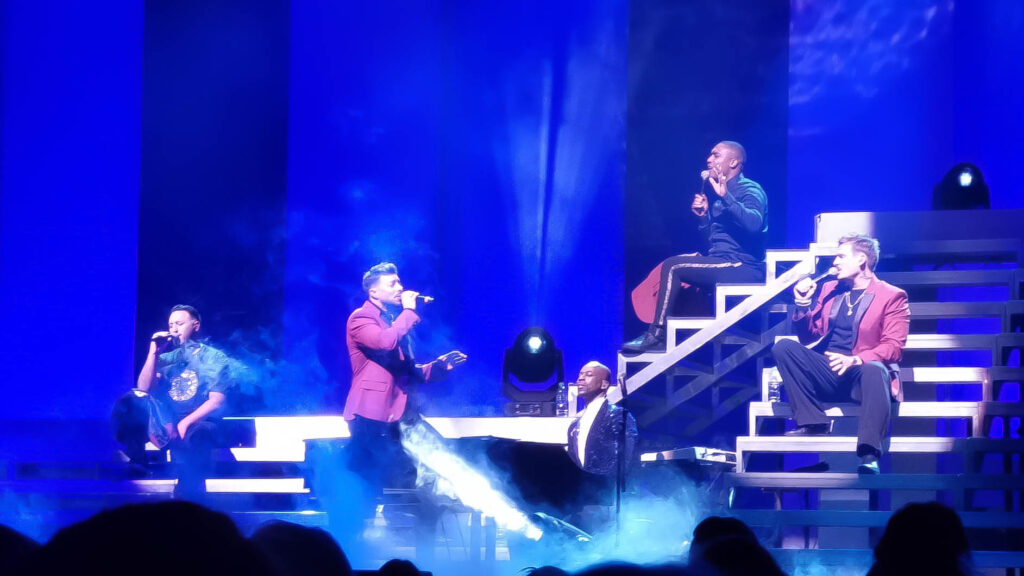 heart & soul - the four members of the band sing on stage, one is sitting on an iron ladder and the others move around with the microphone in hand