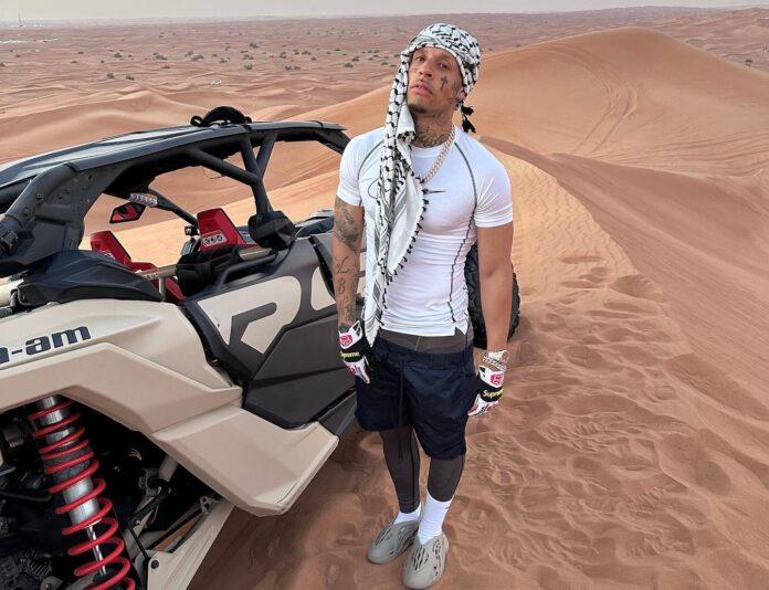 bandito - mambolosco, t shirt bianca, pantaaloni neri e turbante in testa, fotogtafato nel deserto, di fianco a un dune buggt
