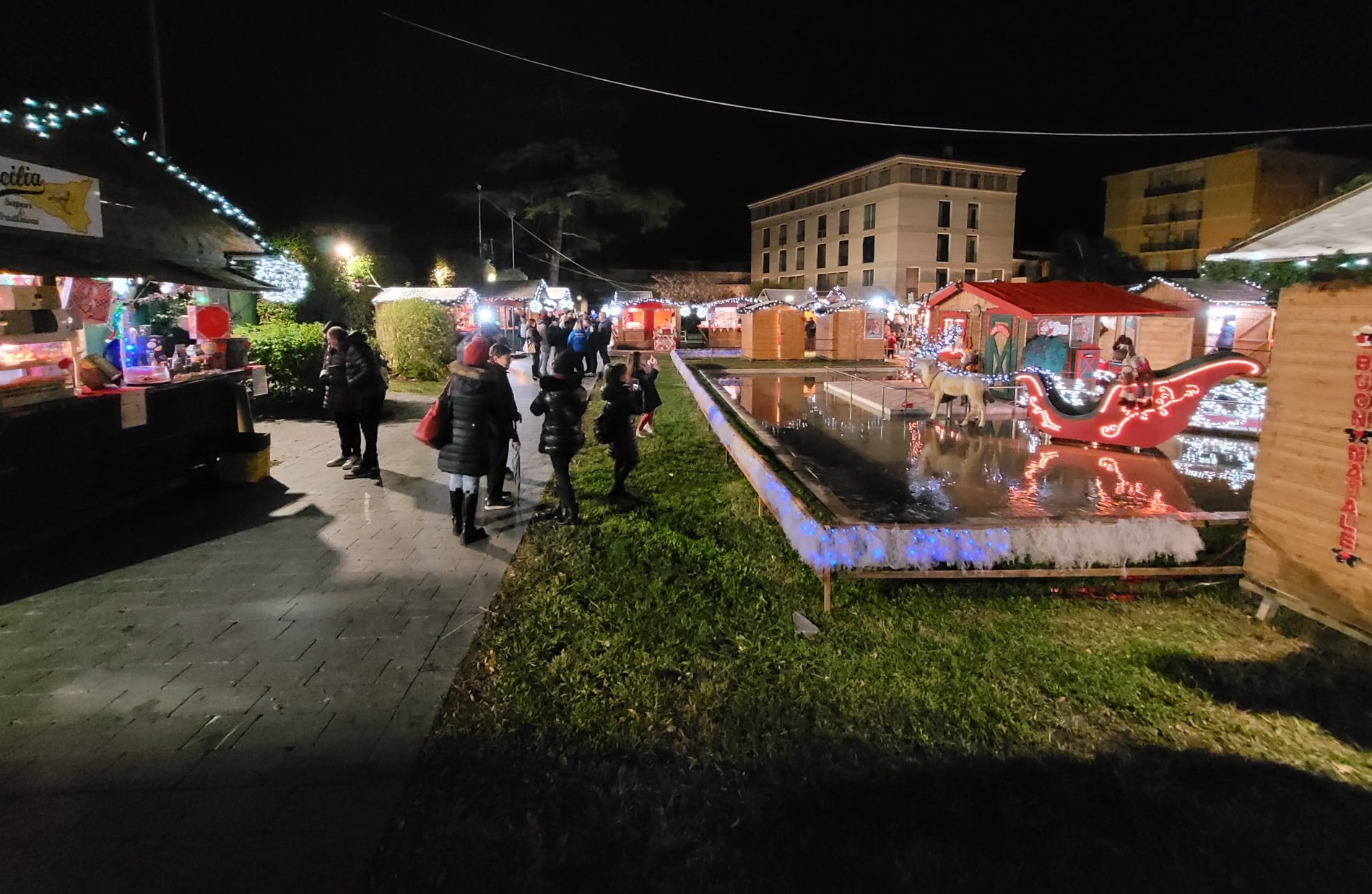 villaggio di natale - della gente cammina in mezzo alle casette rosse illuminate da tante luci colorate