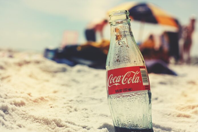 Coca Cola - una bottiglia di vetro di coca cola oncastrata nella sabbia di una spiaggia