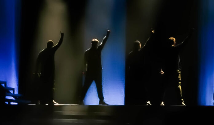 Blue 20th anniversary tour - i 4 componenti della band di schiena sul palco, con il braccio destro alzato, fasci di luce blu e nera tra loro