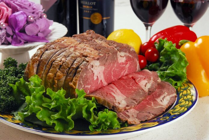 carne e vino nella foto, rappresentate da un bel pezzo di arrosto al sangue tagliato a fette posizionato su un piatto con intorno dell'insalata e sullo sfondo una bottiglia di vino e dei peperoni