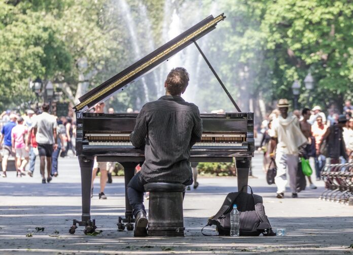 indennità di discontinuità - un piaista suona un pianoforte a coda in mezzo alla strada piena di passanti. il pianista è di schiena