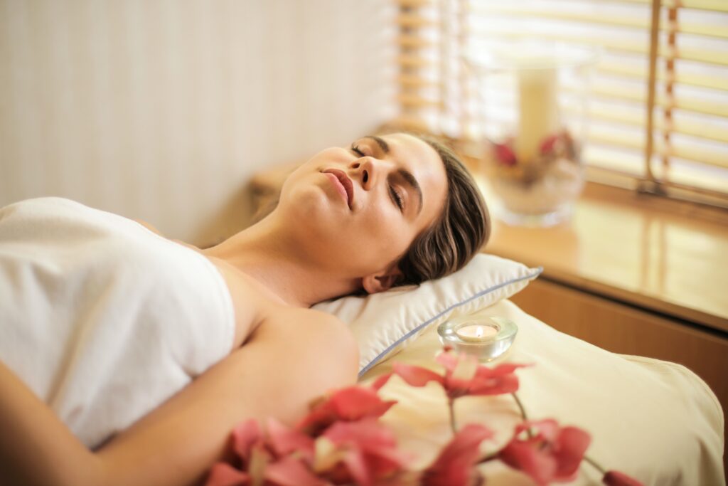 Terme - una donna sdraiata su un lettino massaggi coperta da un asciugamano e di fianco dei fiori colorati