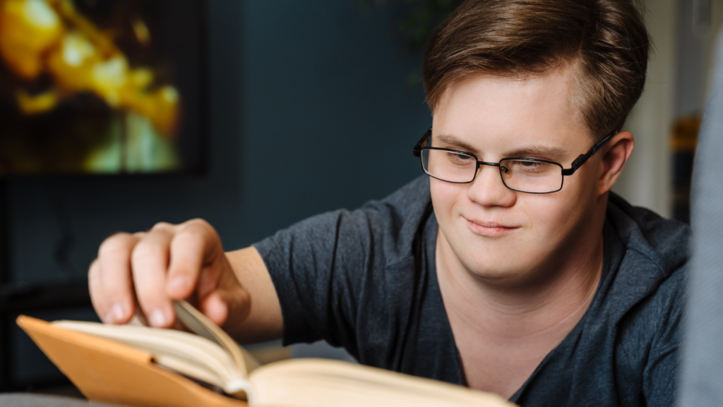 un ragazzo con occhiali con sindrome down seduto daventi a un libro