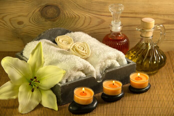 cure termali - nella foto due asciugamani bianchi arrotolati dentro un vassoio vicino, un fiore d'orchidea, davanti tre candele profumate arancioni e due ampolle con olio per massaggi